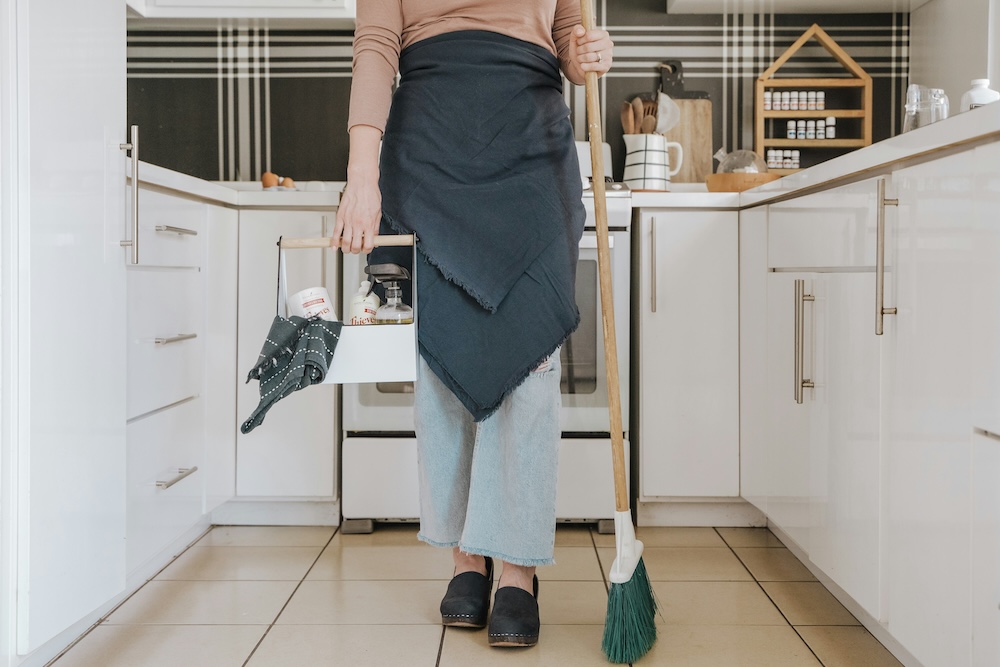 women with broom and cleaning caddy in kitchen